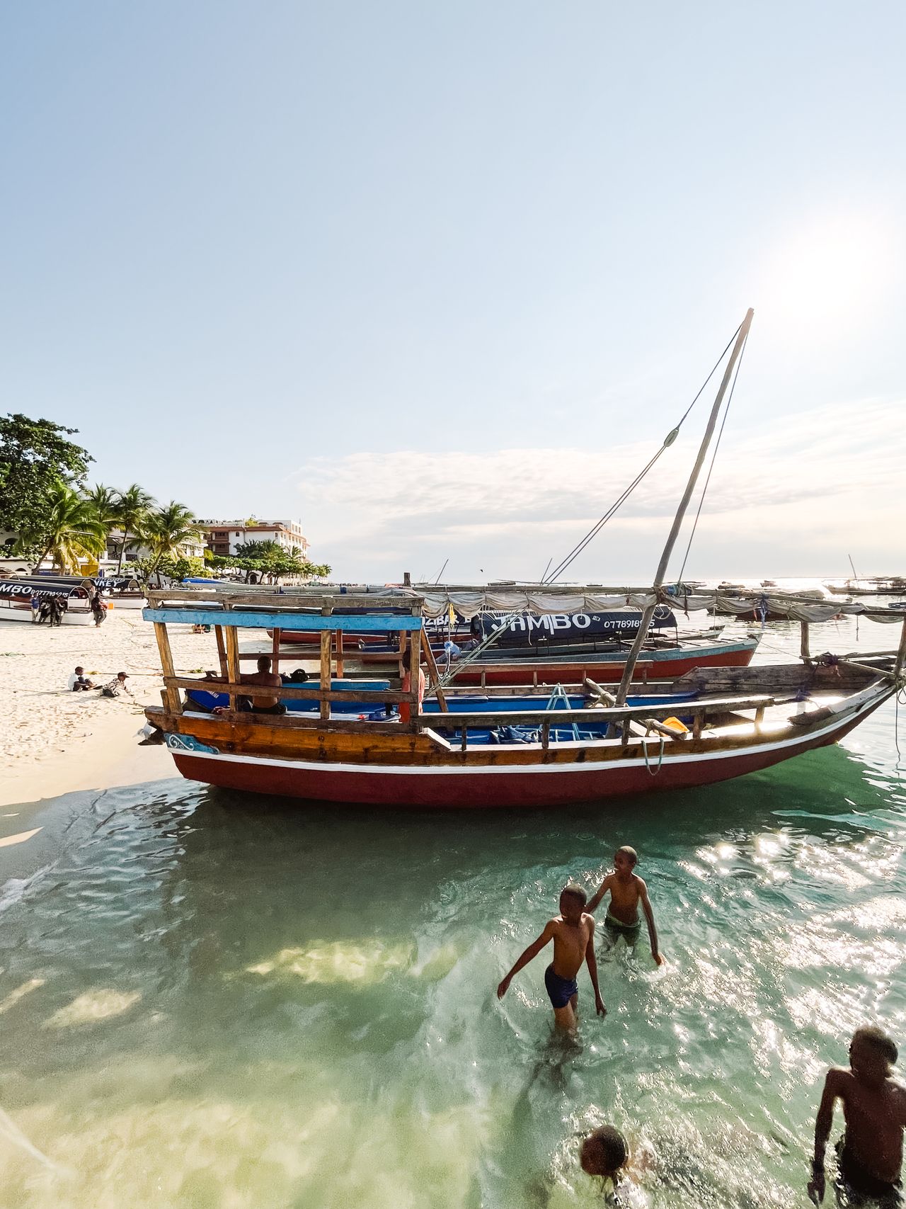 Family-safe beach — children swimming, calm waters, traditional wooden dhow boats at Nungwi