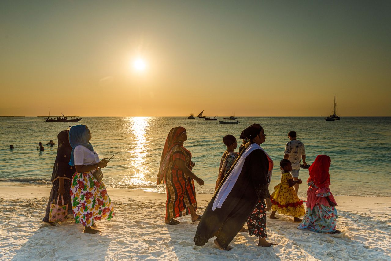 Nungwi beach sunset — local women in colorful dress, white sand, dhow boats on horizon