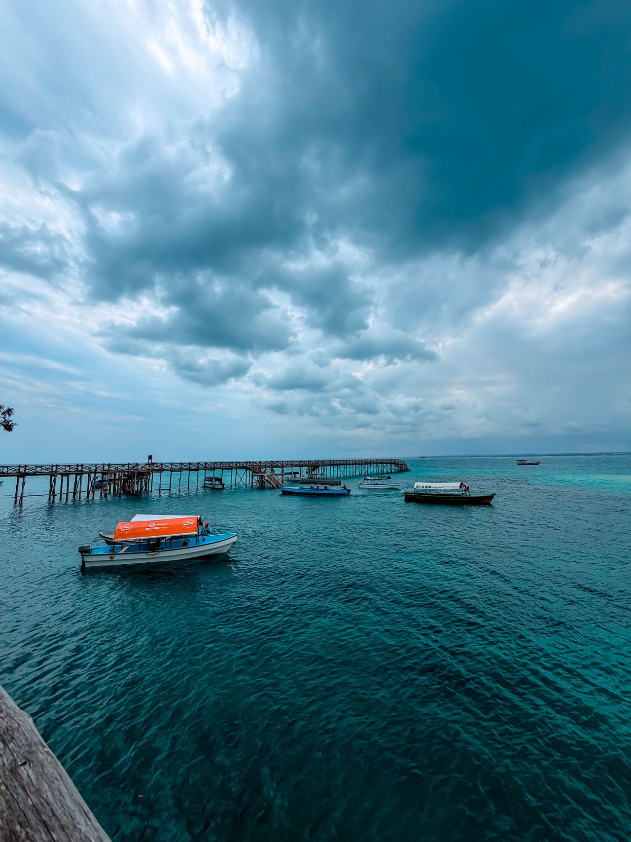 Prison Island wooden pier — motorboats anchored, turquoise Indian Ocean, cloudy sky