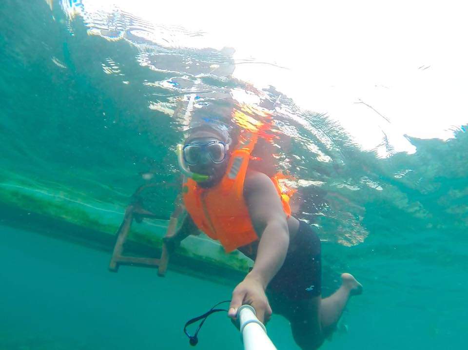 Person snorkeling underwater with orange life vest and mask, near a boat ladder