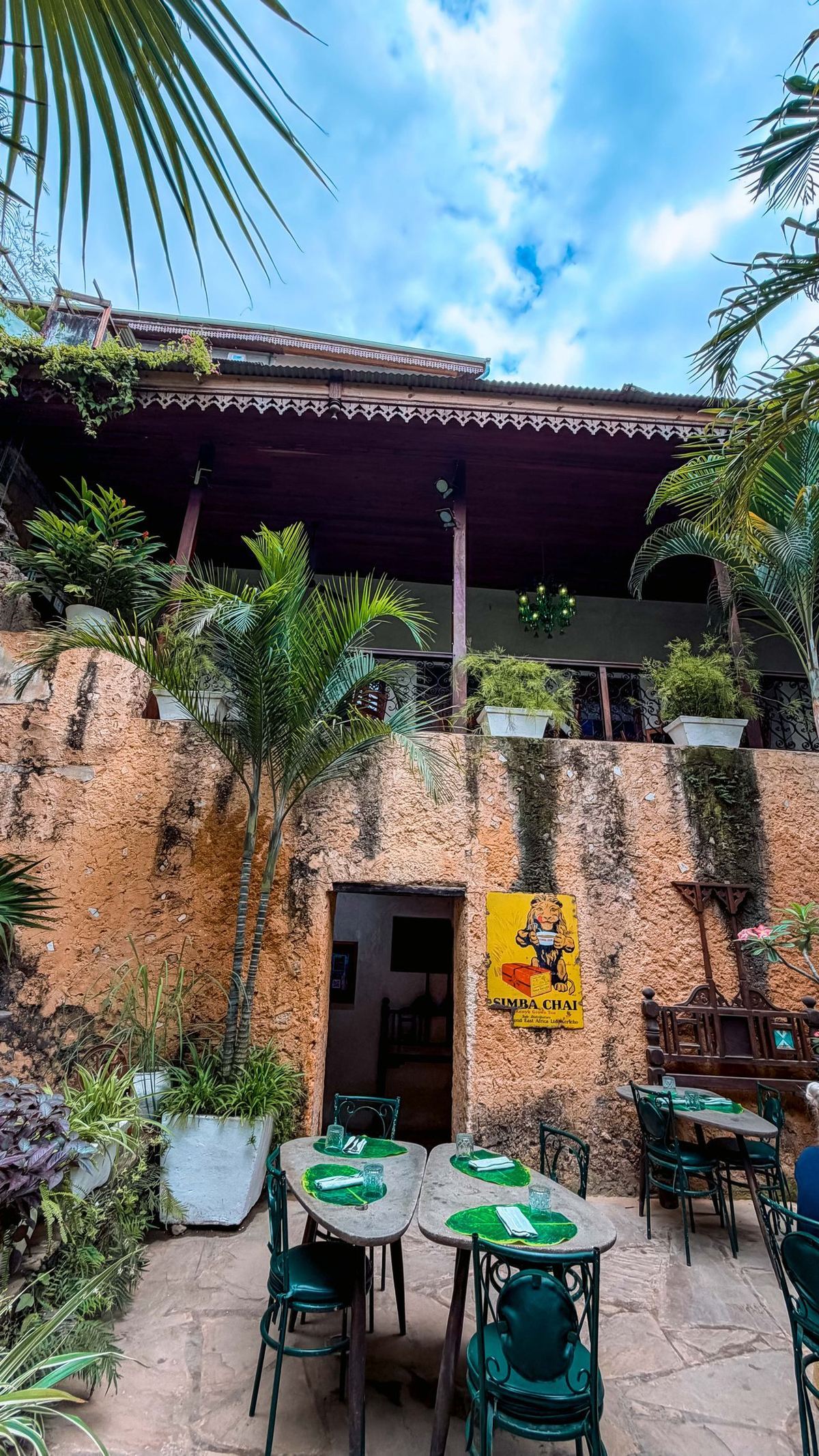 Stone Town historic restaurant courtyard — stone walls, tropical palm plants, open-air dining tables