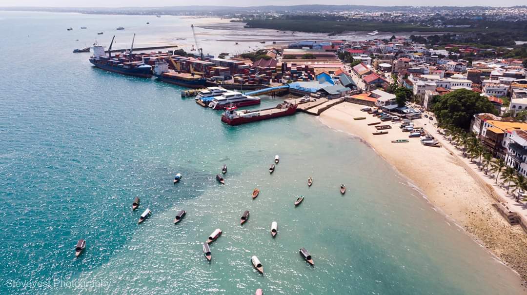 Zanzibar Stone Town port with cargo ships and ferries, and a sandy beach with traditional boats