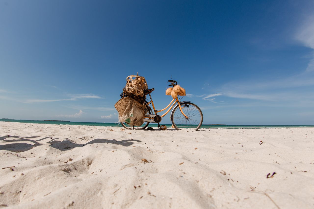 Bicycle on Zanzibar beach — woven baskets, fresh coconuts, white sand, blue sky