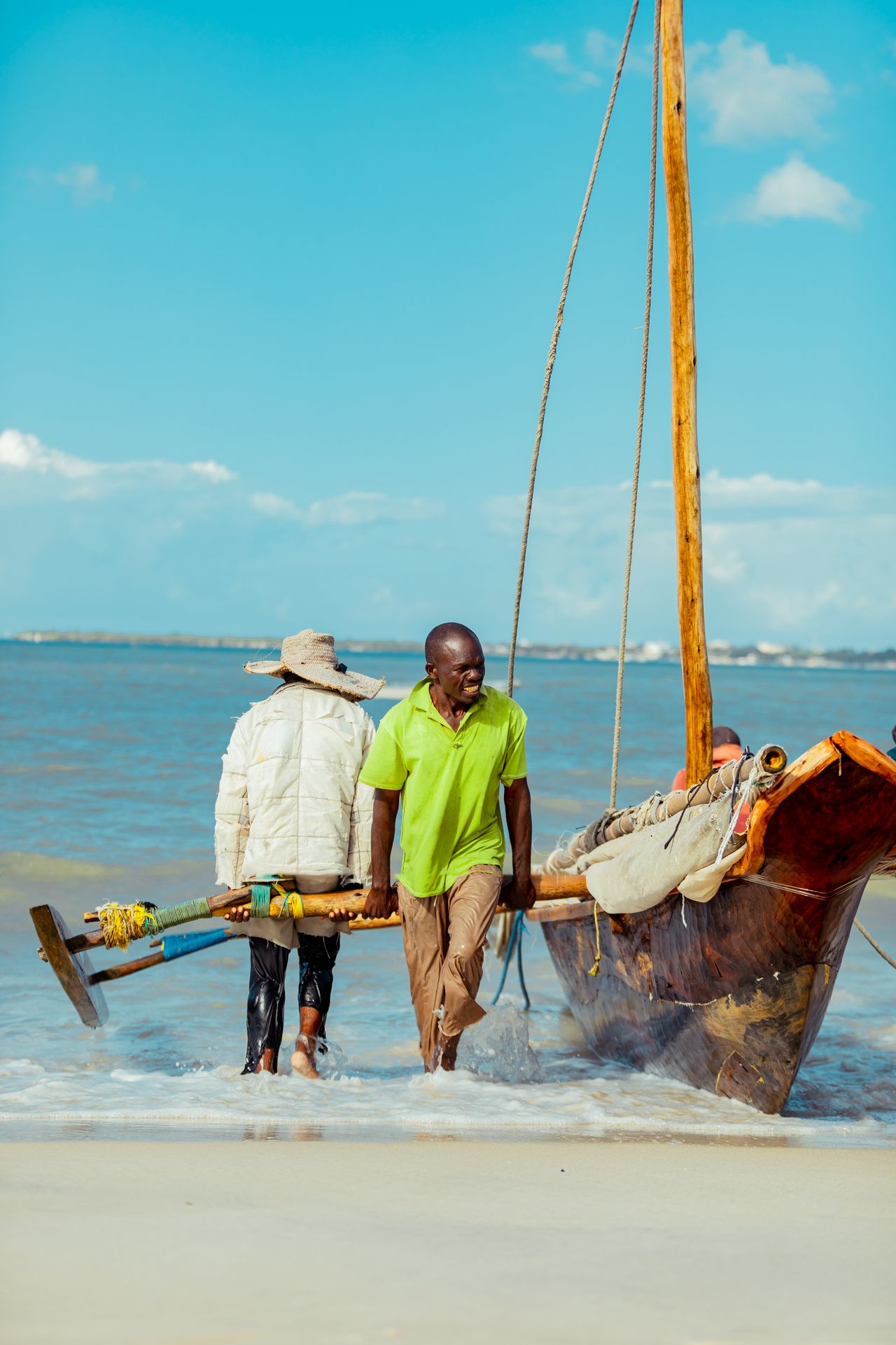 Fishermen with traditional ngalawa boat — outrigger canoe, wooden mast, turquoise ocean, Nungwi beach