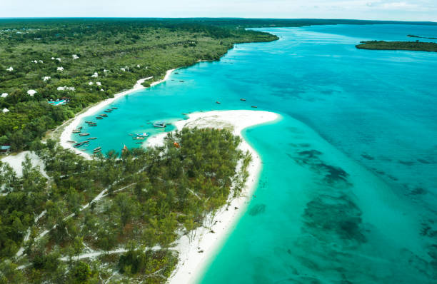 Fumba beach aerial view — white sand peninsula, turquoise Indian Ocean, lush green vegetation, traditional boats