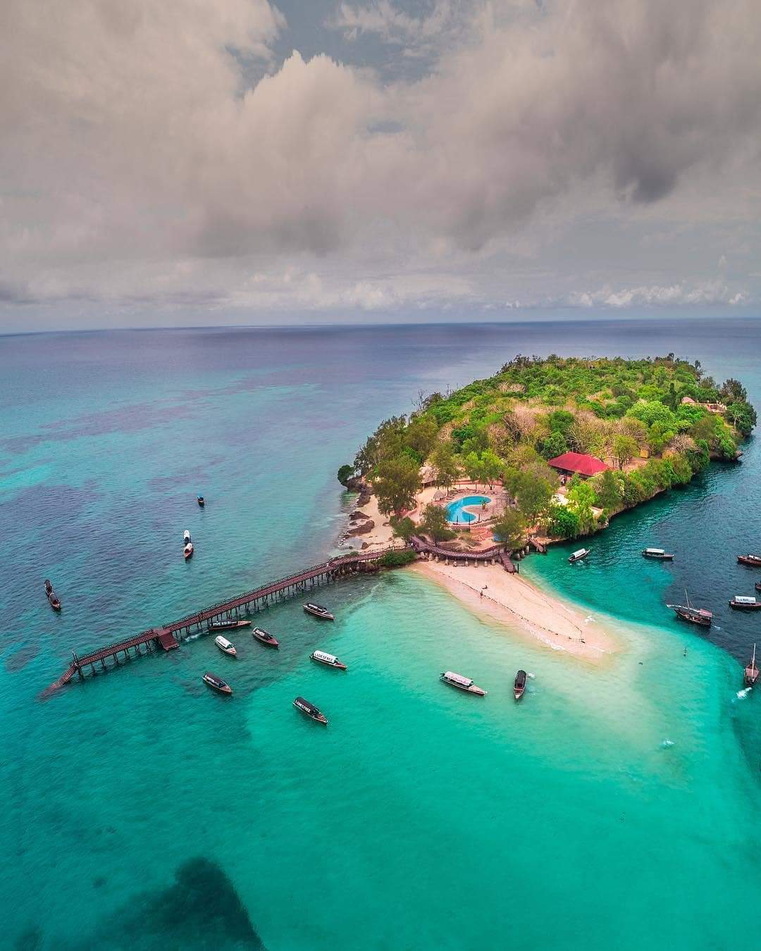 Zanzibar island resort — turquoise water, sandy beach, wooden pier, boats, swimming pool