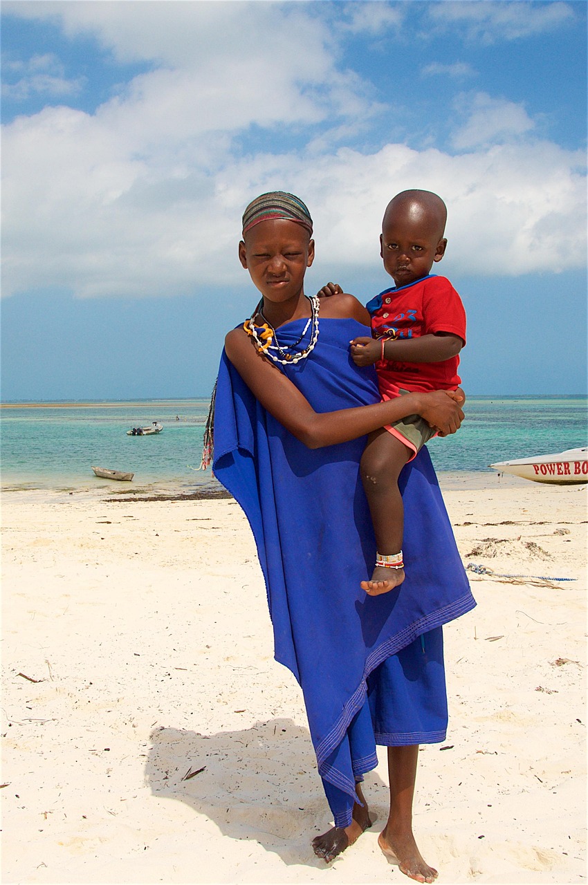 Zanzibar local children on beach — young girl carrying toddler, traditional attire, white sand
