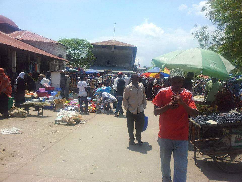 Zanzibar market scene — people shopping, stalls with goods, traditional buildings