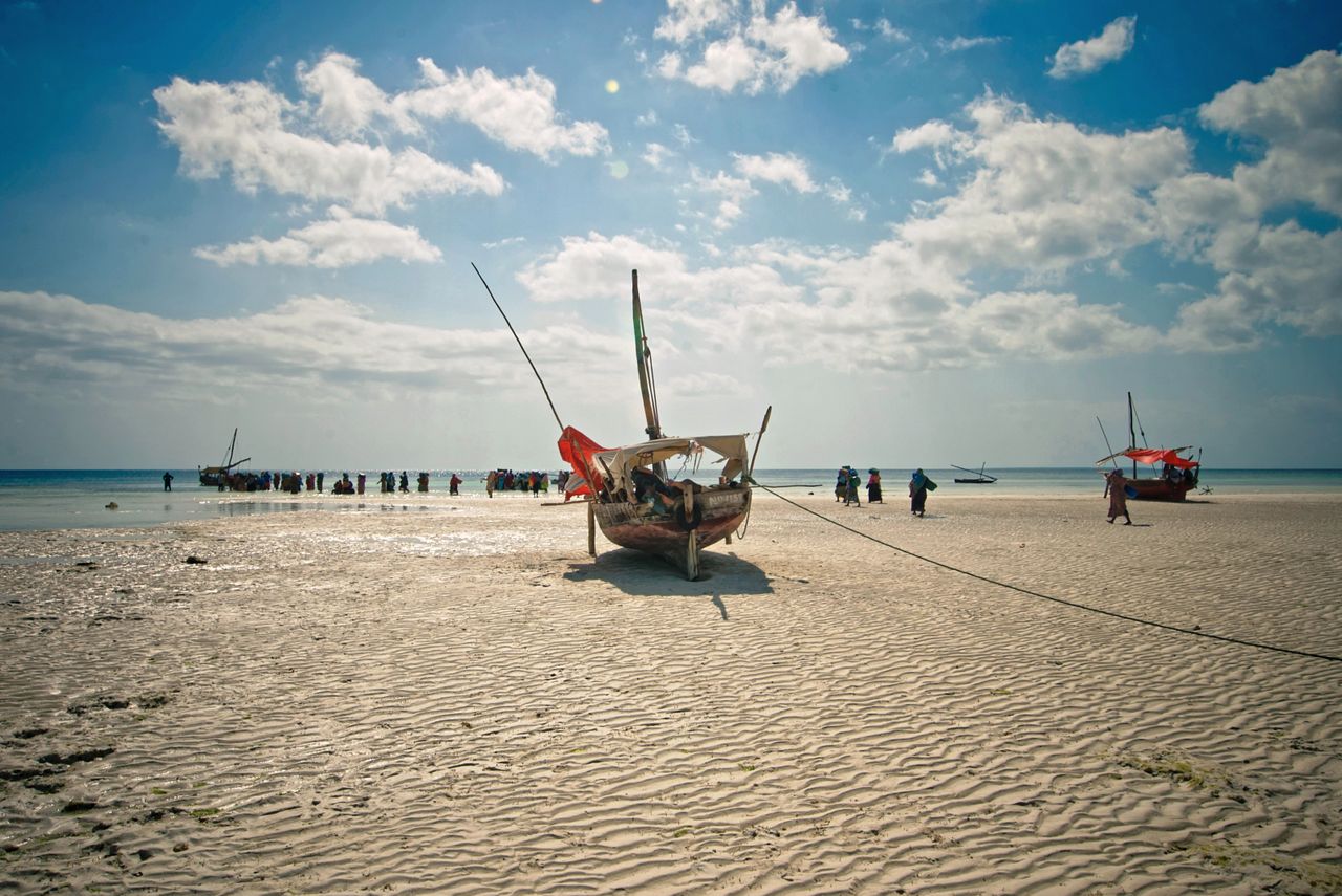 Traditional fishing boats at low tide — white sand ripples, local villagers, blue sky with clouds
