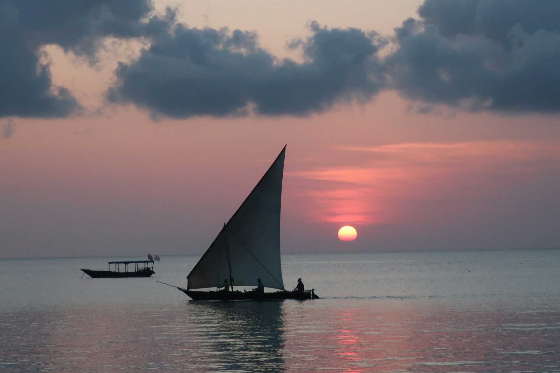 Traditional dhow at sunset — silhouette against orange sky, calm Indian Ocean, Nungwi coast