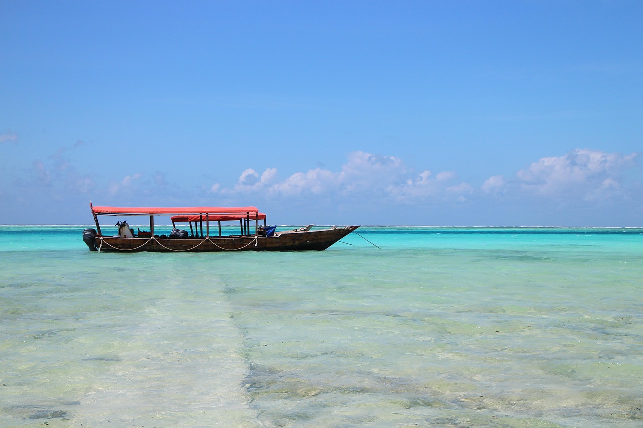 Traditional wooden boat in Zanzibar — red canopy, turquoise Indian Ocean, clear shallow water